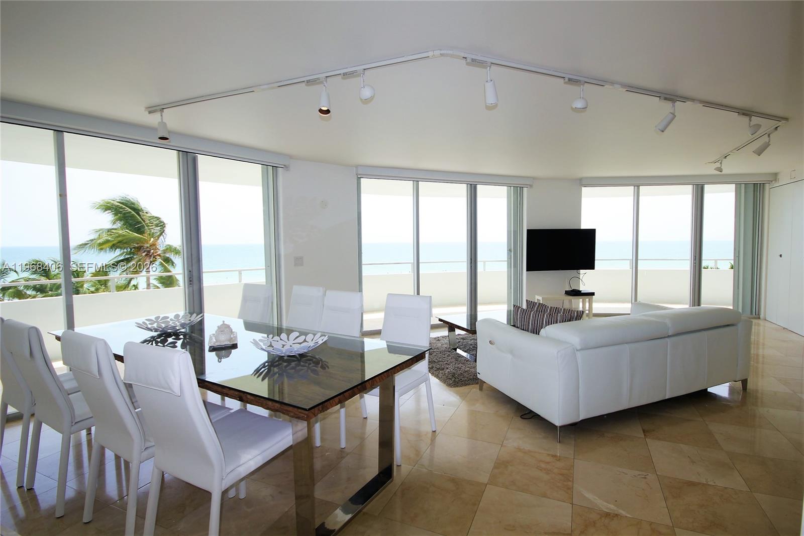 A dining and living area features white furniture, tile floors, track lighting, and ocean views — 5151 COLLINS AV # 532, Miami Beach FL 33140, MIAMI BEACH, FL