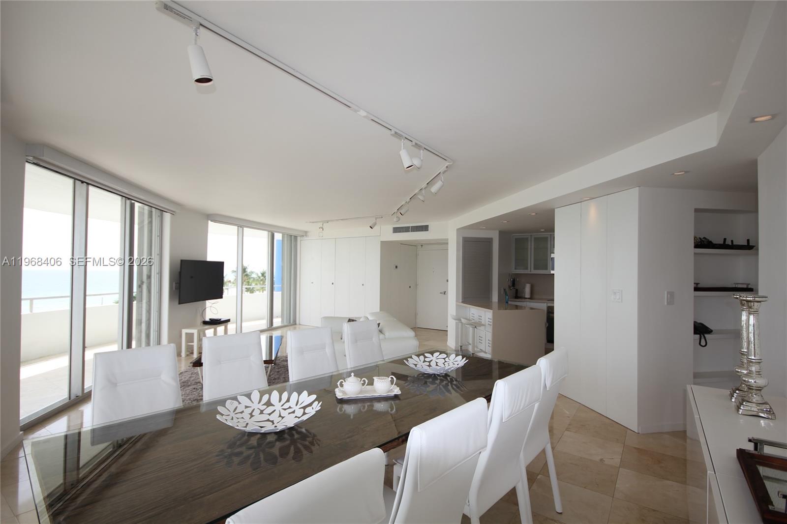 A dining area with a glass table and white chairs opens to a living space — 5151 COLLINS AV # 532, Miami Beach FL 33140, MIAMI BEACH, FL