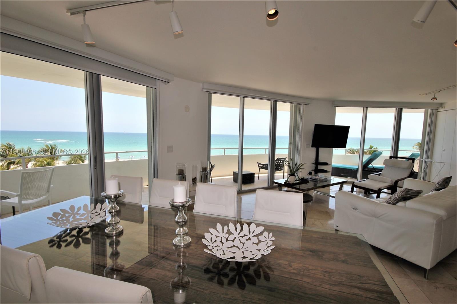A dining and living area features floor-to-ceiling windows with ocean views and white furniture — 5151 COLLINS AV # 532, Miami Beach FL 33140, MIAMI BEACH, FL
