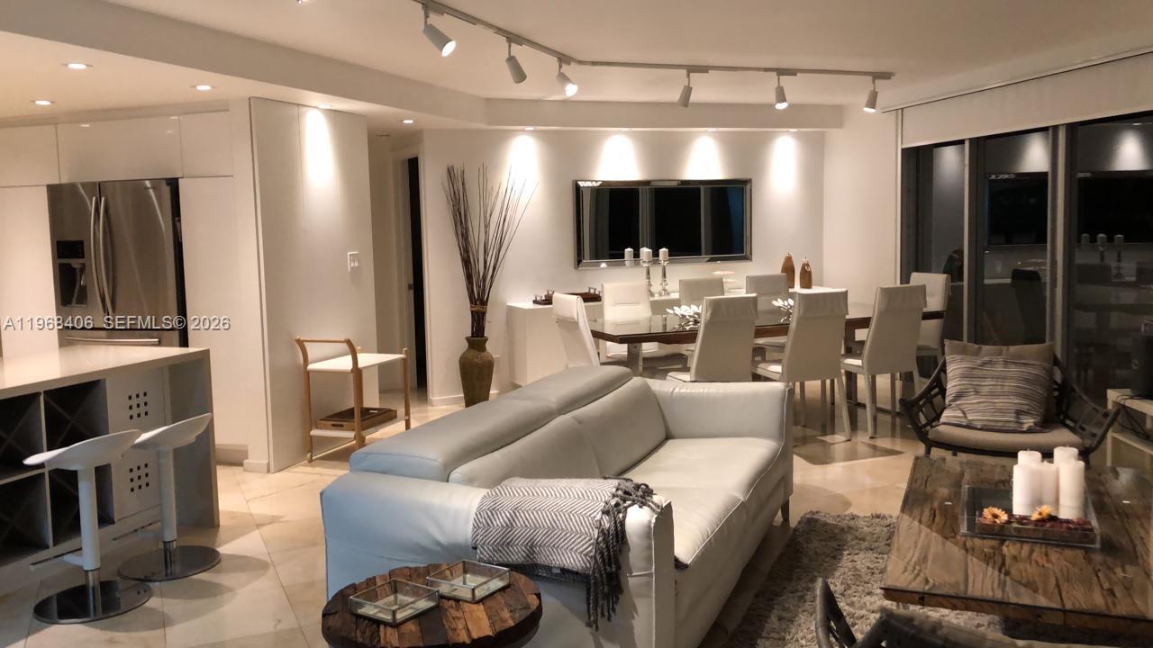 A modern open-plan living and dining area features white furniture, track lighting, and tile flooring — 5151 COLLINS AV # 532, Miami Beach FL 33140, MIAMI BEACH, FL