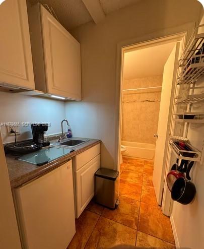A small kitchen area with white cabinets, a sink, and a doorway leading to a bathroom — 2306 Liberty St # C, Hollywood FL 33020, HOLLYWOOD, FL