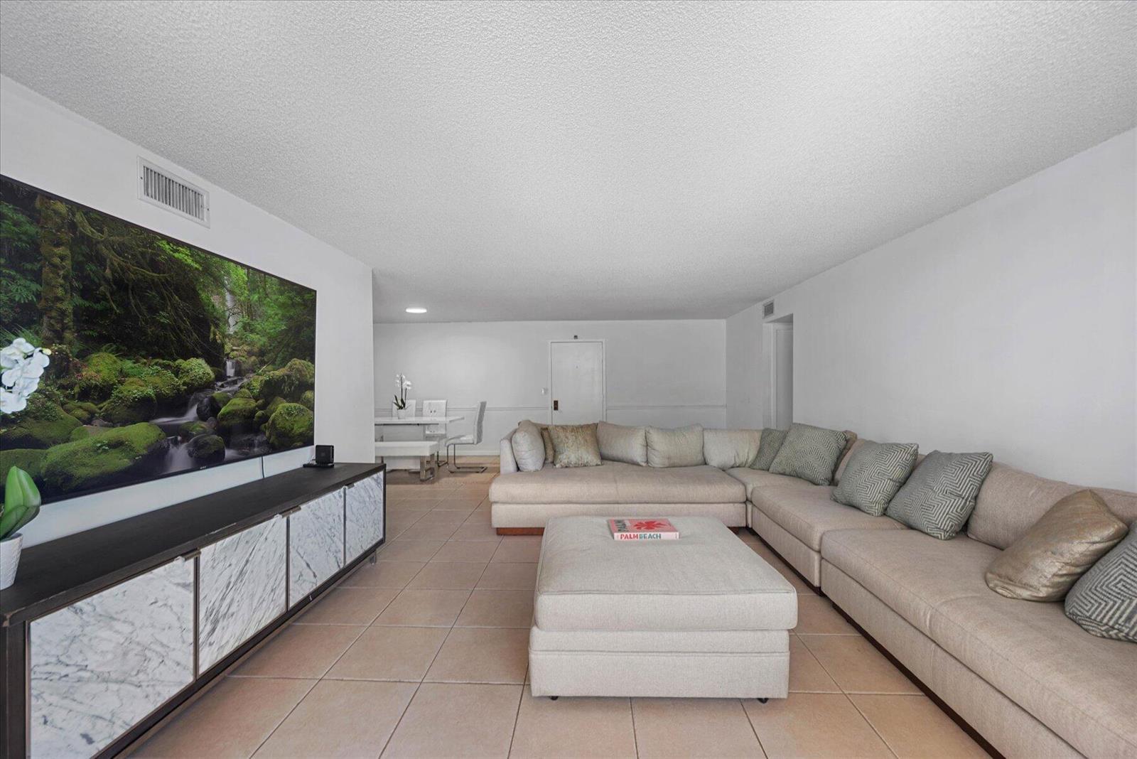 A living room features a large television, a marble media console, and a beige sectional — 3200 S Ocean Boulevard # A102, Palm Beach FL 33480, PALM BEACH, FL