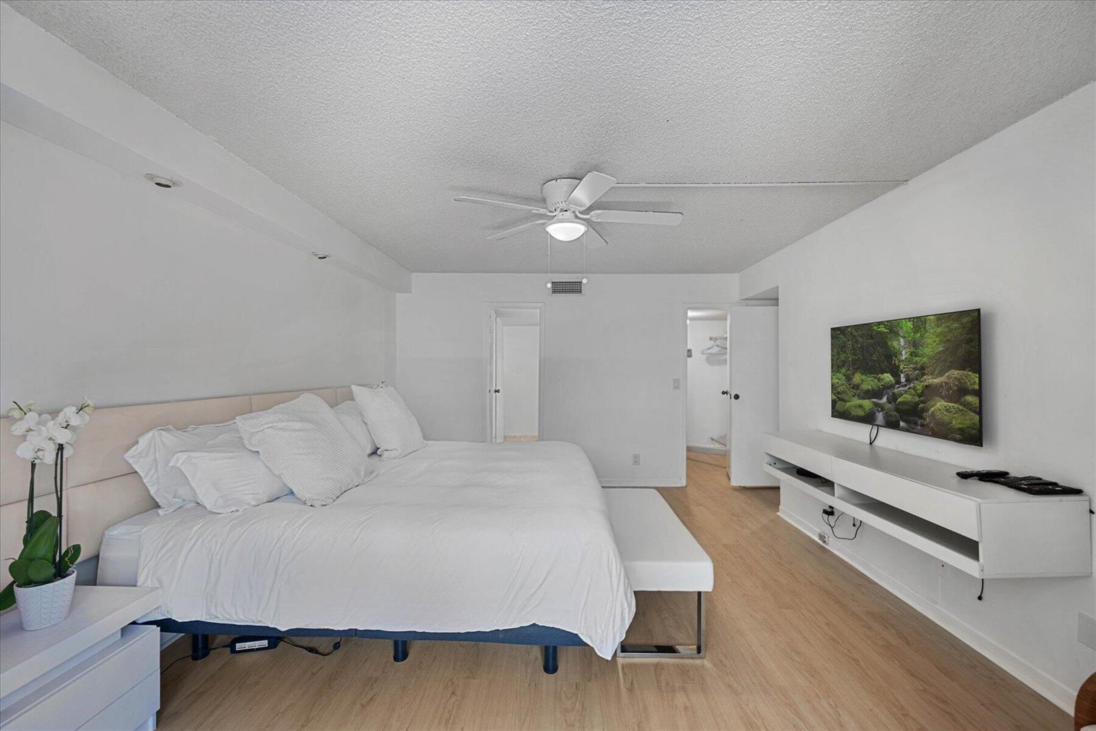 A bedroom features a large bed, a wall-mounted television, and light wood-look flooring — 3200 S Ocean Boulevard # A102, Palm Beach FL 33480, PALM BEACH, FL