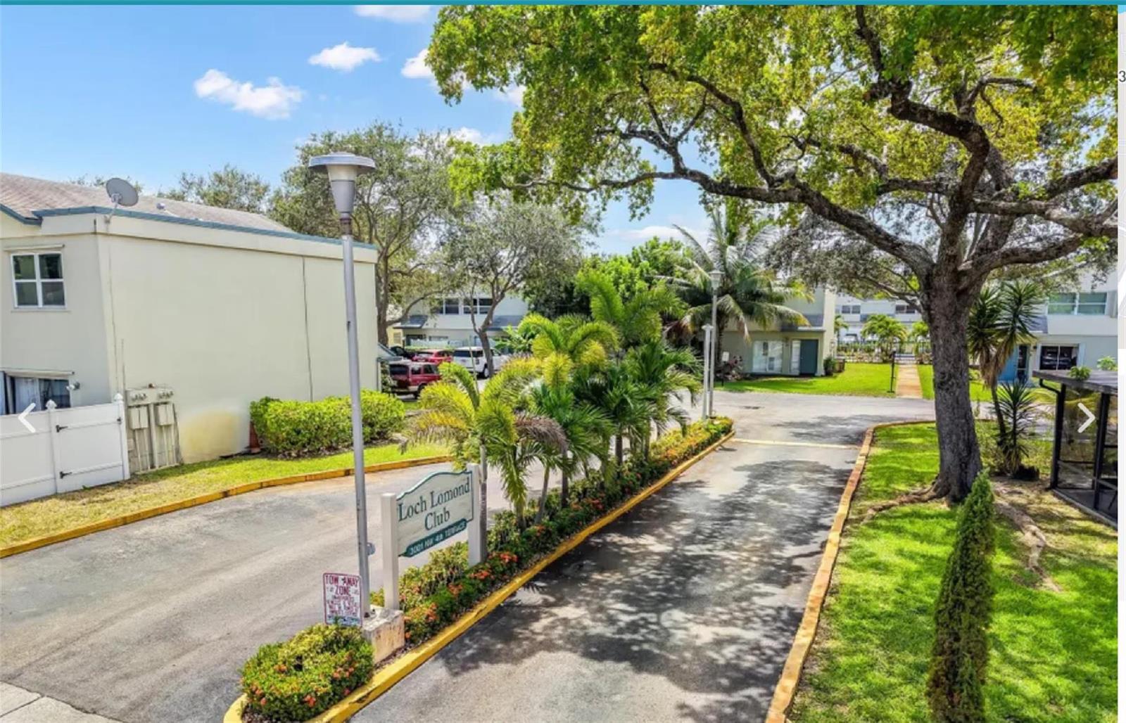 An exterior view of the Loch Lomond Club entrance with a sign, trees, and driveway — 3001 NW 4th Terrace # 152, Pompano Beach FL 33064, POMPANO BEACH, FL