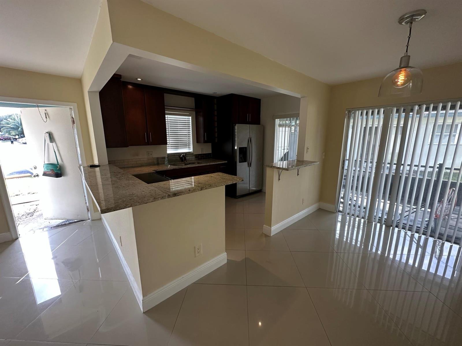 A kitchen with dark wood cabinets, granite countertops, and tile flooring opens to a dining area — 3001 NW 4th Terrace # 152, Pompano Beach FL 33064, POMPANO BEACH, FL