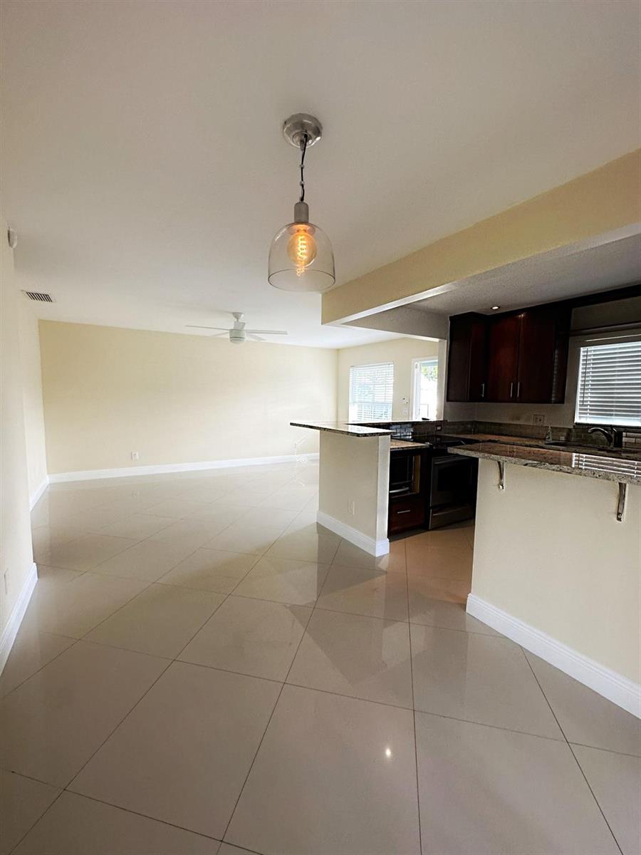 A kitchen with dark cabinets and granite countertops opens into a spacious, tiled living area — 3001 NW 4th Terrace # 152, Pompano Beach FL 33064, POMPANO BEACH, FL