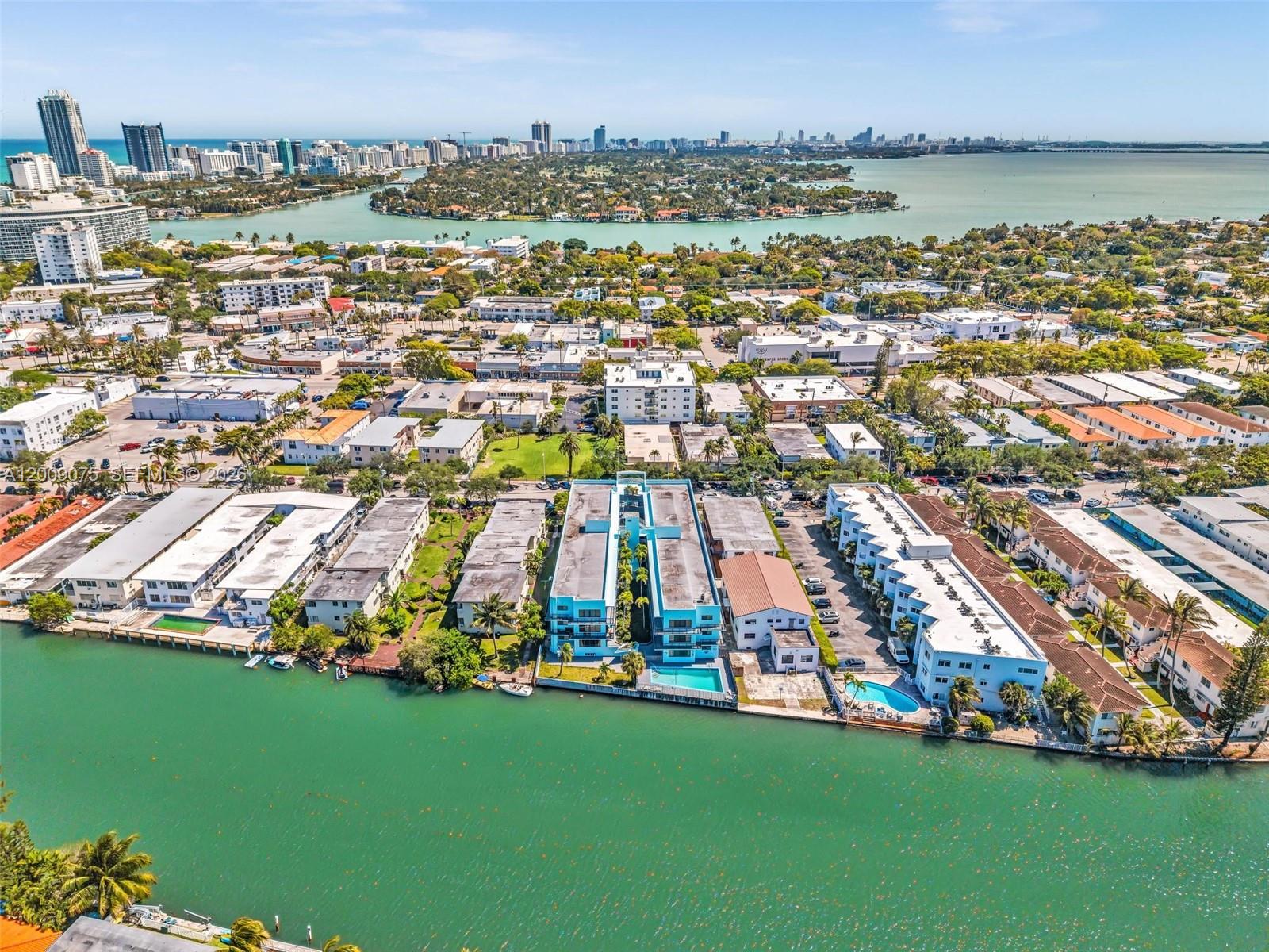An aerial view shows waterfront apartment buildings with swimming pools along a canal — 1165 Marseille Dr # 4, Miami Beach FL 33141, MIAMI BEACH, FL