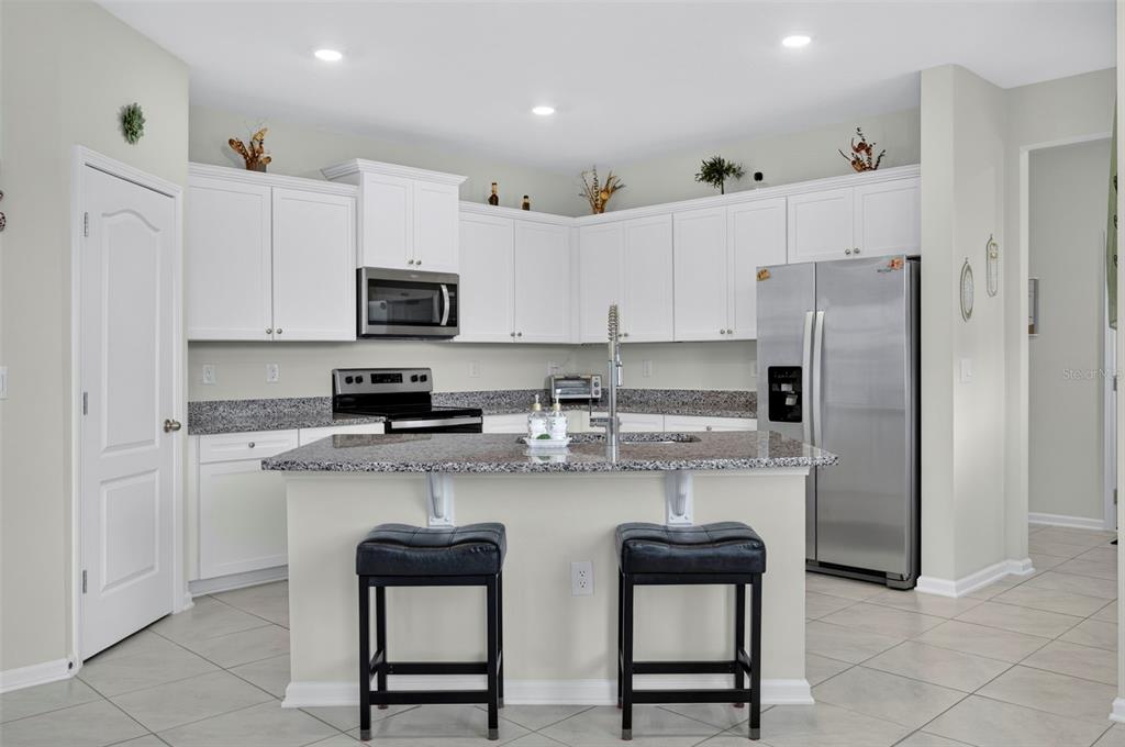 A kitchen features white cabinetry, granite countertops, a central island with two stools, and stainless appliances — 122 REDBUD ROAD, PALM COAST, FL