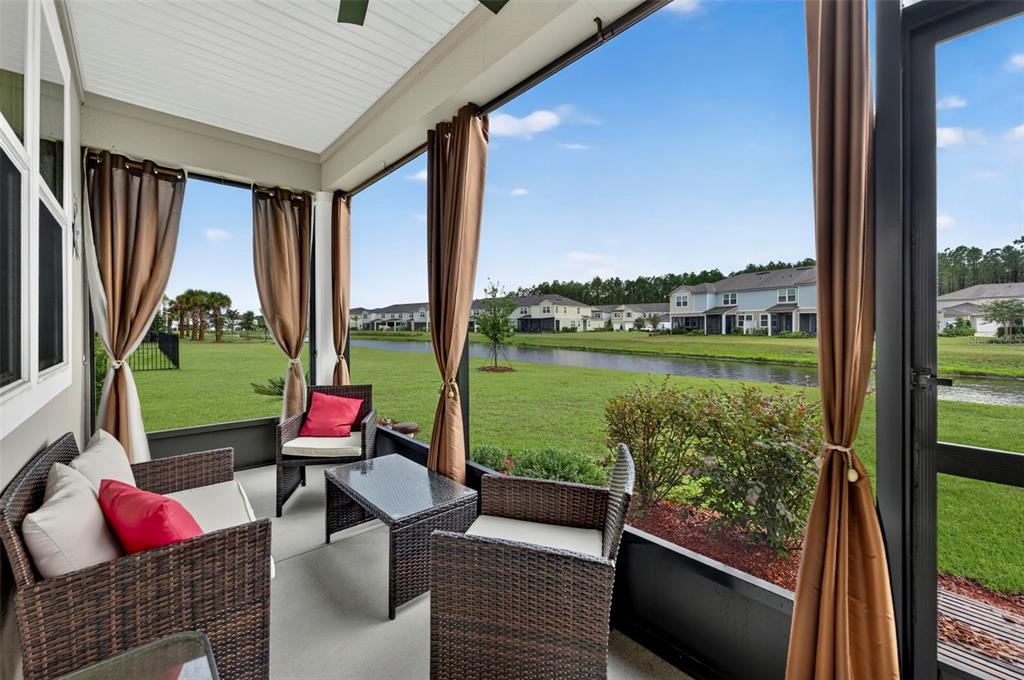 A screened-in patio with wicker furniture overlooks a grassy lawn and a small canal — 122 REDBUD ROAD, PALM COAST, FL