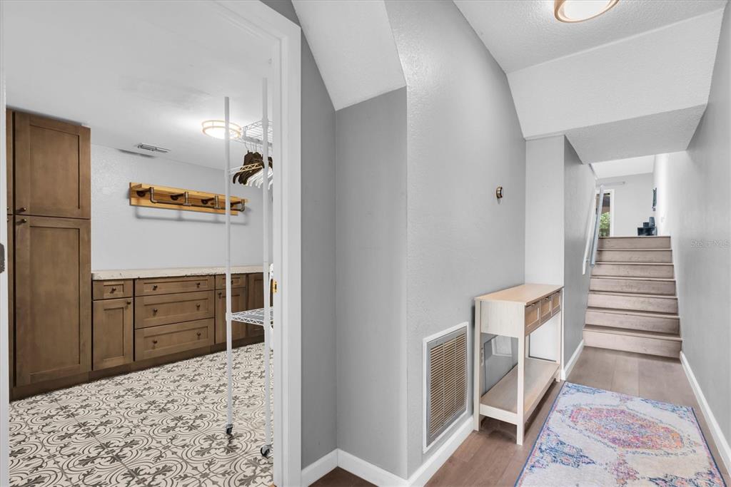 A hallway with a patterned tile laundry room, a console table, and a staircase — 6494 92ND PLACE N UNIT 203, PINELLAS PARK, FL