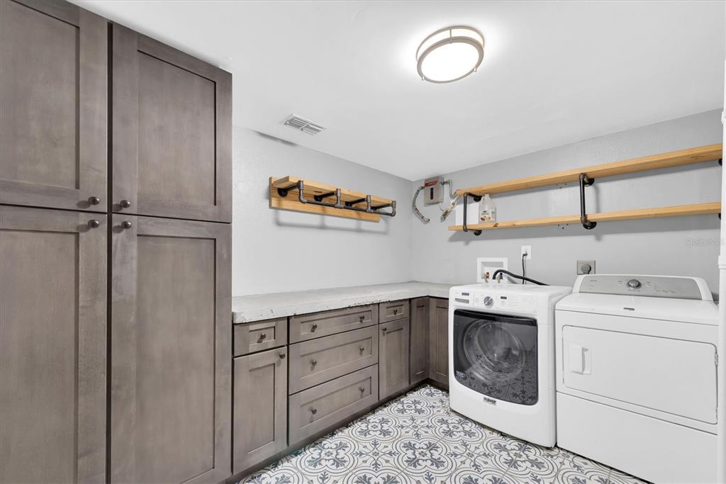 A laundry room features gray cabinets, a concrete countertop, patterned tile flooring, and open shelving — 6494 92ND PLACE N UNIT 203, PINELLAS PARK, FL