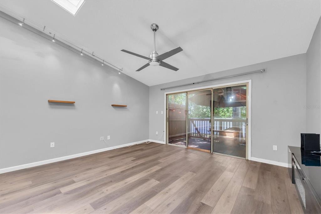 A living room features light gray walls, wood-look flooring, a ceiling fan, and sliding glass doors — 6494 92ND PLACE N UNIT 203, PINELLAS PARK, FL