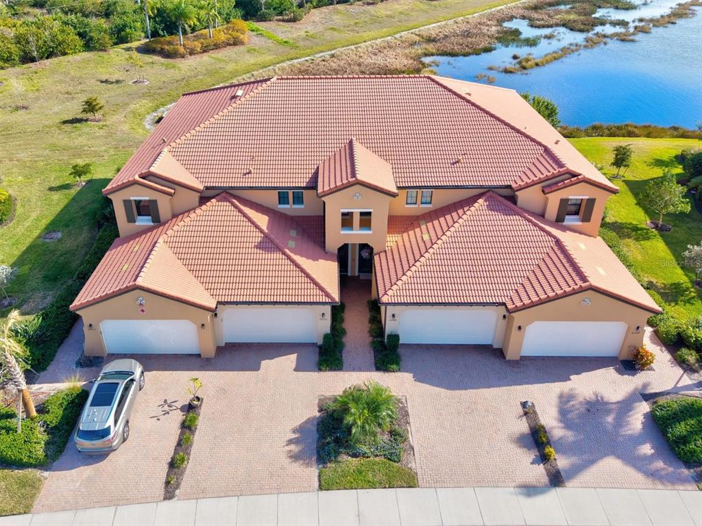 An exterior view of a two-story tan building with a tiled roof and screened balconies — 23516 AWABUKI DRIVE UNIT 201, VENICE, FL