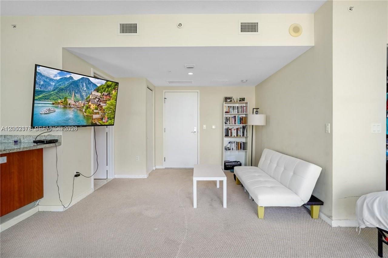 A living room features a white sofa, a coffee table, a bookshelf, and a wall-mounted television — 185 SW 7th St # 3100, Miami FL 33130, MIAMI, FL