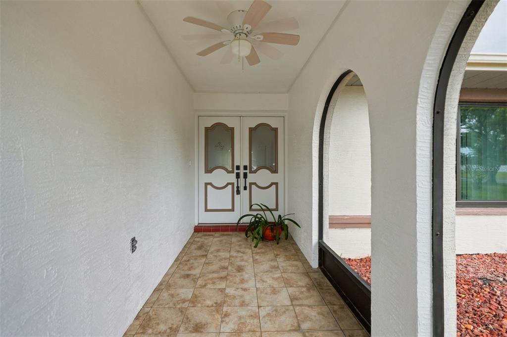 A covered entryway features a tiled floor, a ceiling fan, and double doors with glass inserts — 10308 GIFFORD DRIVE, SPRING HILL, FL