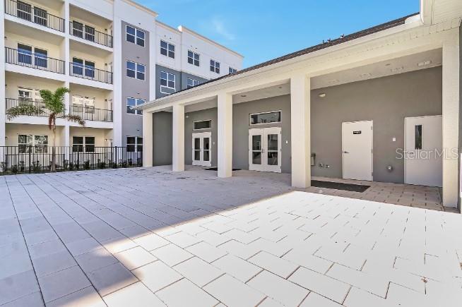 A paved patio area sits in front of a modern apartment building with white doors — 1230 SOUTHSTATION PLACE UNIT 104, ORLANDO, FL