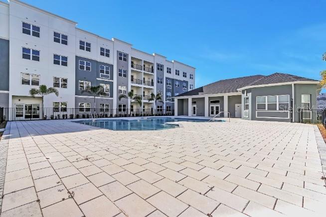 A swimming pool sits on a paved patio beside a multi-story apartment building — 1230 SOUTHSTATION PLACE UNIT 104, ORLANDO, FL