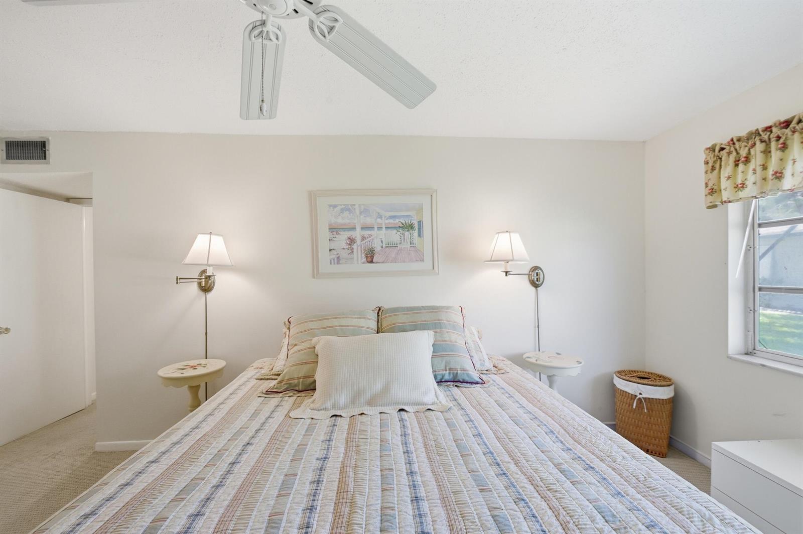 A bedroom features a bed with striped bedding, wall-mounted lamps, and a ceiling fan — 940 S Drive Terrace # A, Delray Beach FL 33445, DELRAY BEACH, FL