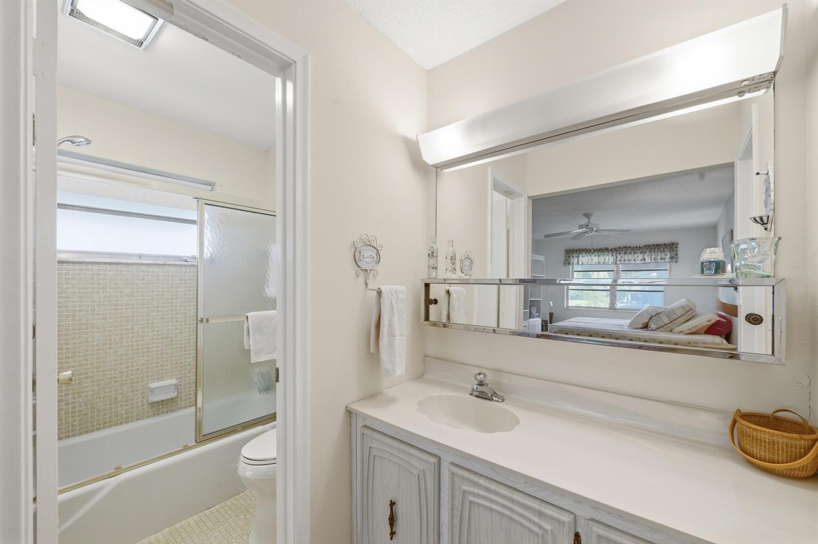 A bathroom features a white vanity, a large mirror, and an adjacent tub-shower combination — 940 S Drive Terrace # A, Delray Beach FL 33445, DELRAY BEACH, FL