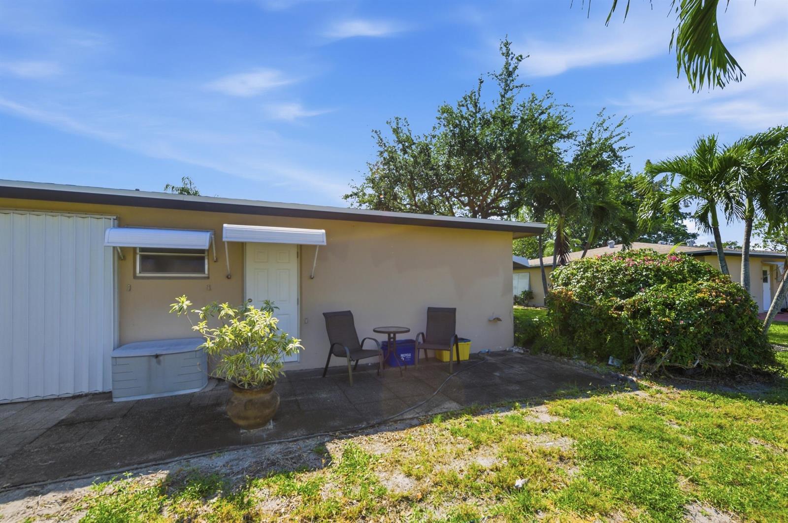 A beige exterior wall features a door, a window, and a small patio with chairs — 940 S Drive Terrace # A, Delray Beach FL 33445, DELRAY BEACH, FL
