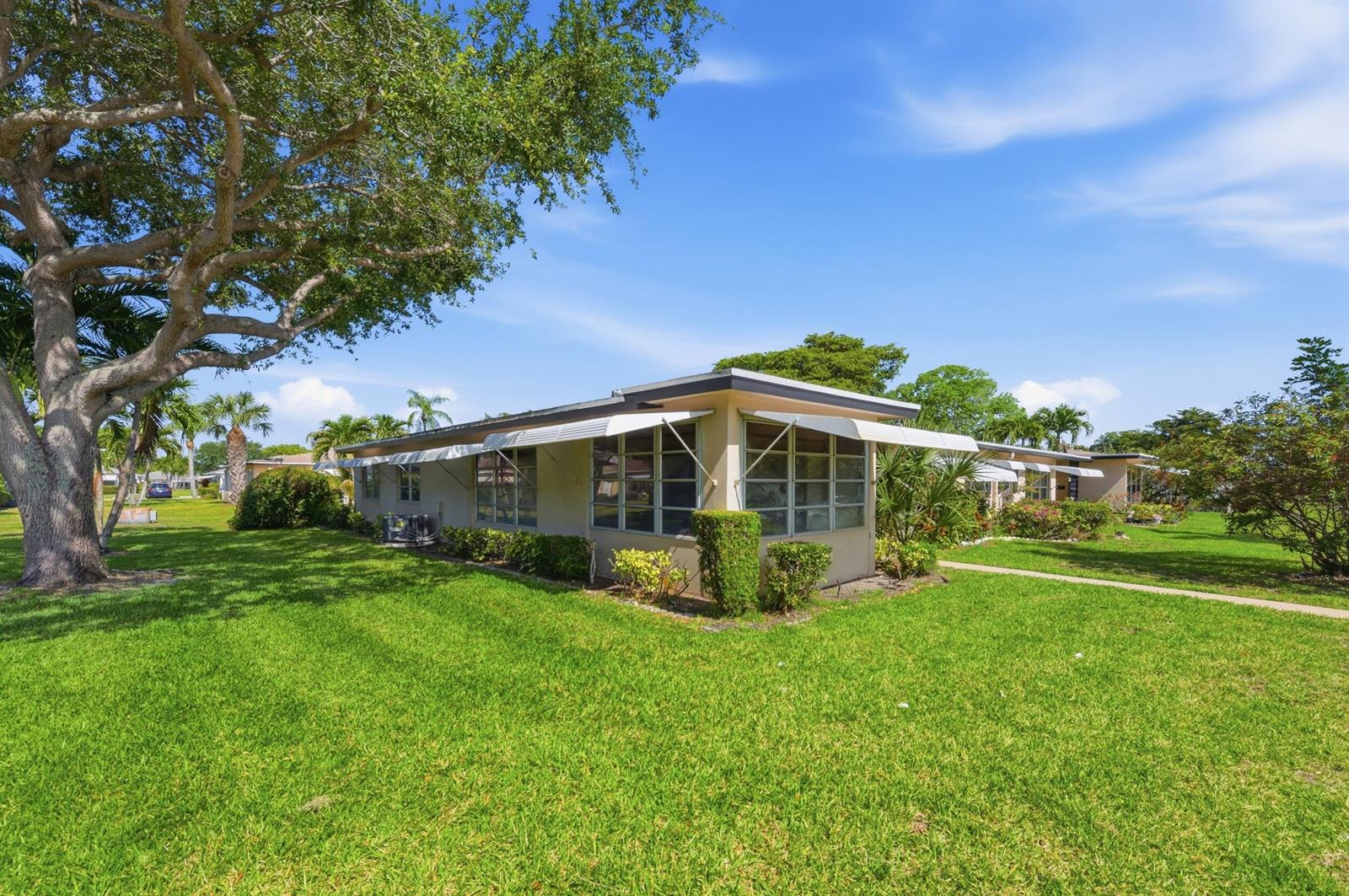 A single-story house with a flat roof and metal awnings sits on a grassy lawn — 940 S Drive Terrace # A, Delray Beach FL 33445, DELRAY BEACH, FL