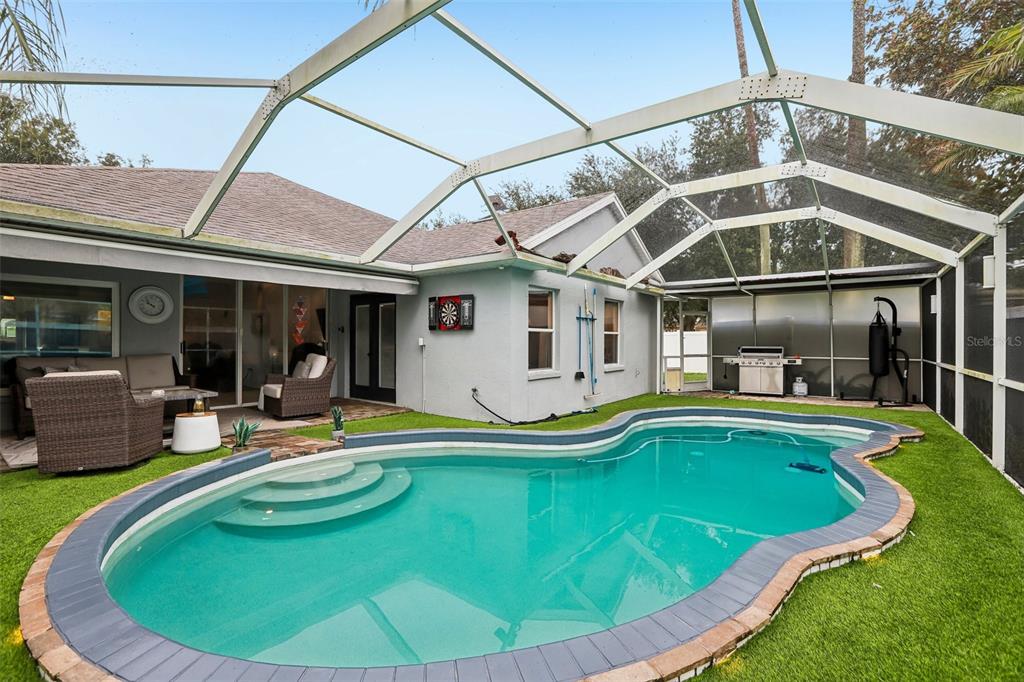 A screened-in patio features a swimming pool, artificial turf, outdoor furniture, and a grill — 19009 FALCONS PLACE, TAMPA, FL