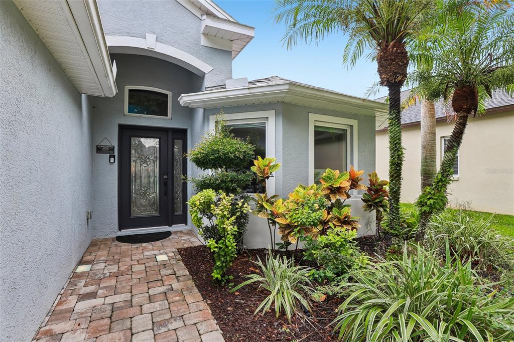 A paved walkway leads to the front entrance of a light blue house with landscaping — 19009 FALCONS PLACE, TAMPA, FL
