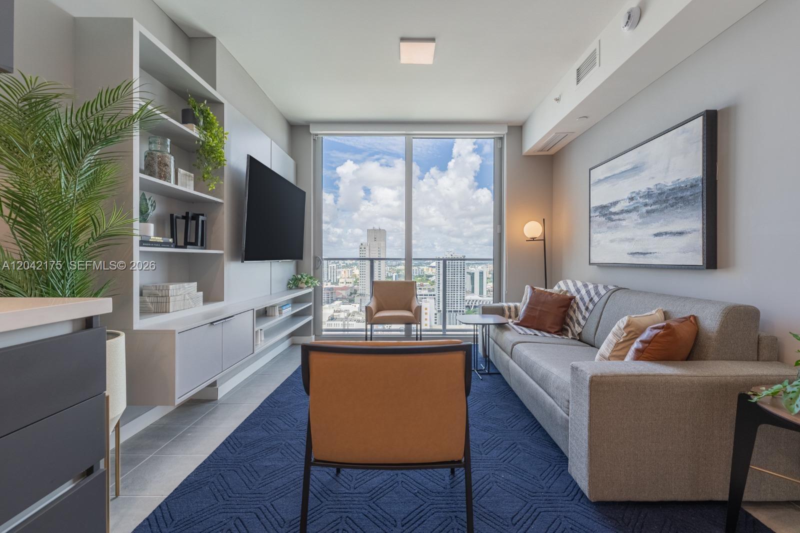 A modern living room features a grey sofa, blue area rug, and floor-to-ceiling windows — 227 NE 2nd St # 3104, Miami FL 33132, MIAMI, FL
