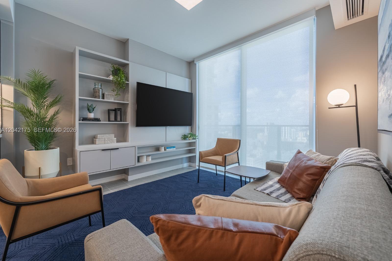 A living room features a blue rug, a wall-mounted television, and two tan accent chairs — 227 NE 2nd St # 3104, Miami FL 33132, MIAMI, FL