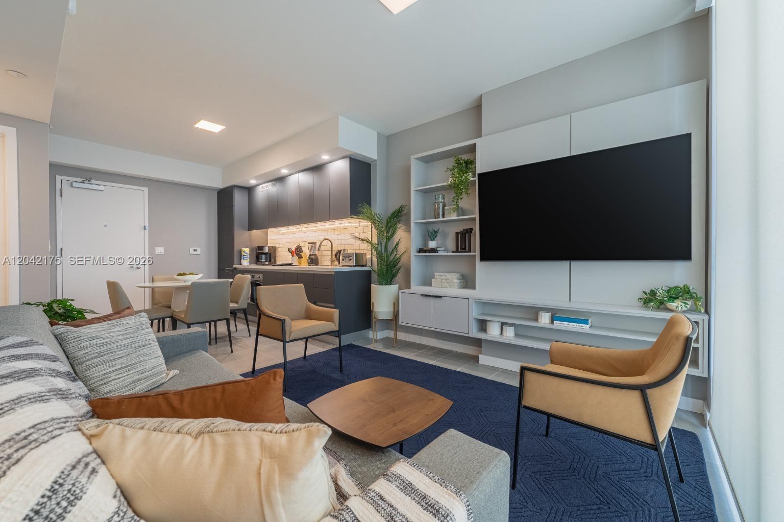 A modern living room features a grey sofa, blue area rug, and an integrated kitchen — 227 NE 2nd St # 3104, Miami FL 33132, MIAMI, FL