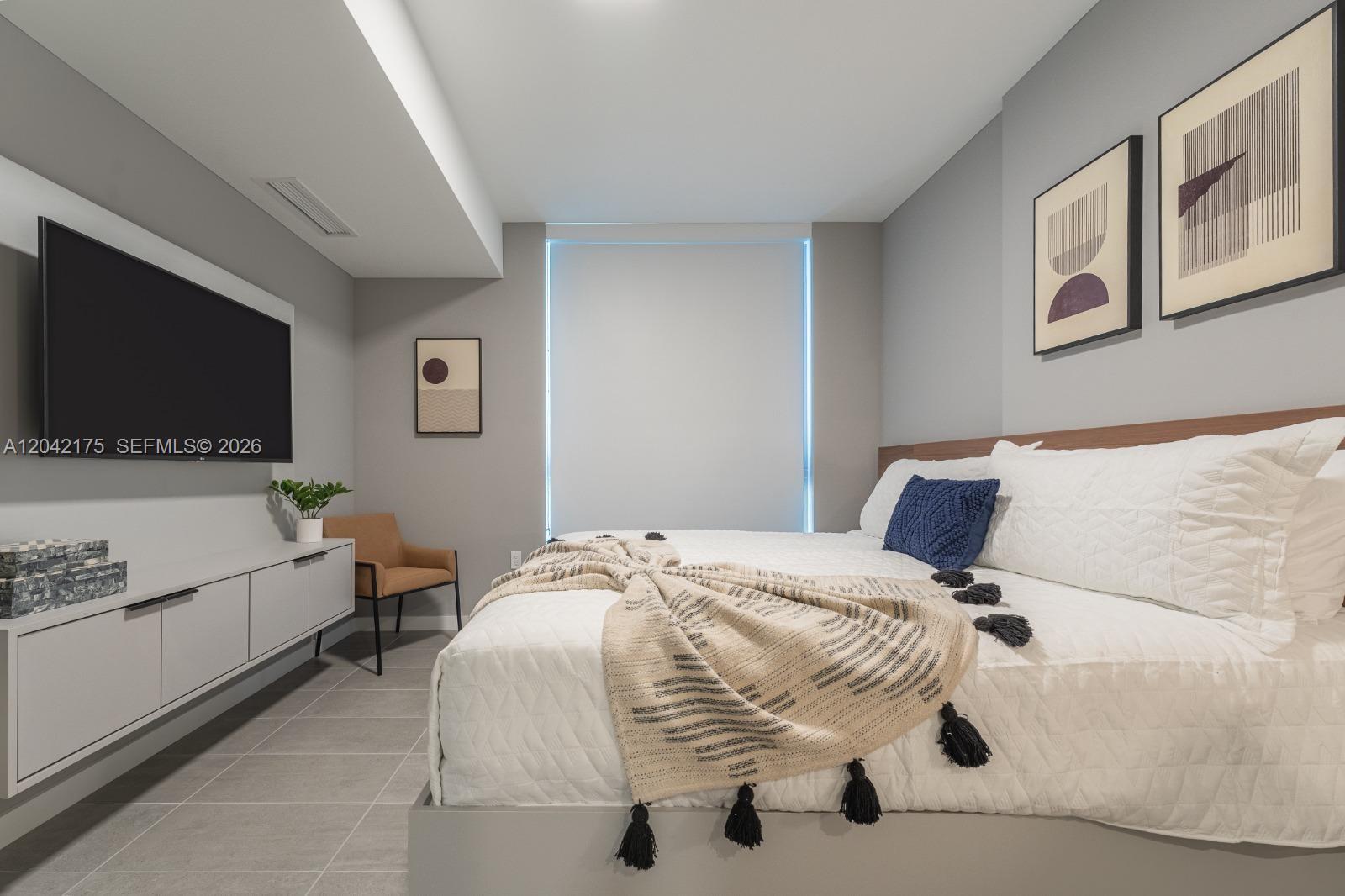 A modern bedroom features a bed with a white quilt, a wall-mounted television, and artwork — 227 NE 2nd St # 3104, Miami FL 33132, MIAMI, FL