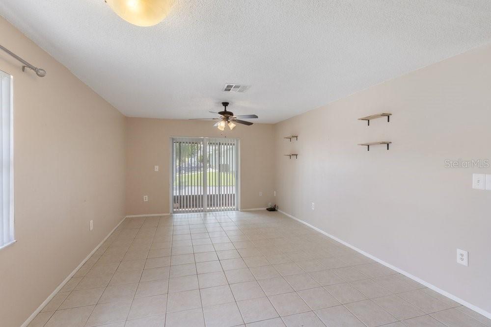 An empty room features light-colored tile flooring, beige walls, a ceiling fan, and sliding doors — 9224 KEYES PLACE, NEW PORT RICHEY, FL