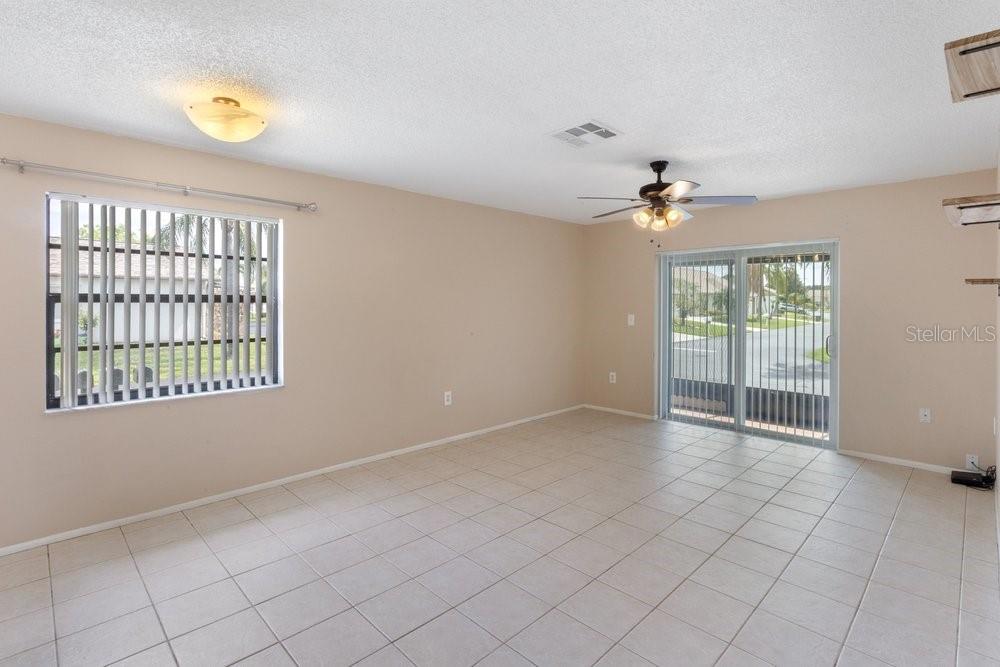 An empty room with beige walls, tile flooring, a ceiling fan, and sliding glass doors — 9224 KEYES PLACE, NEW PORT RICHEY, FL