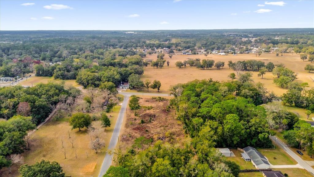 An aerial view shows a rural landscape with a paved road, open fields, and wooded areas — 3653 NE JACKSONVILLE ROAD, OCALA, FL