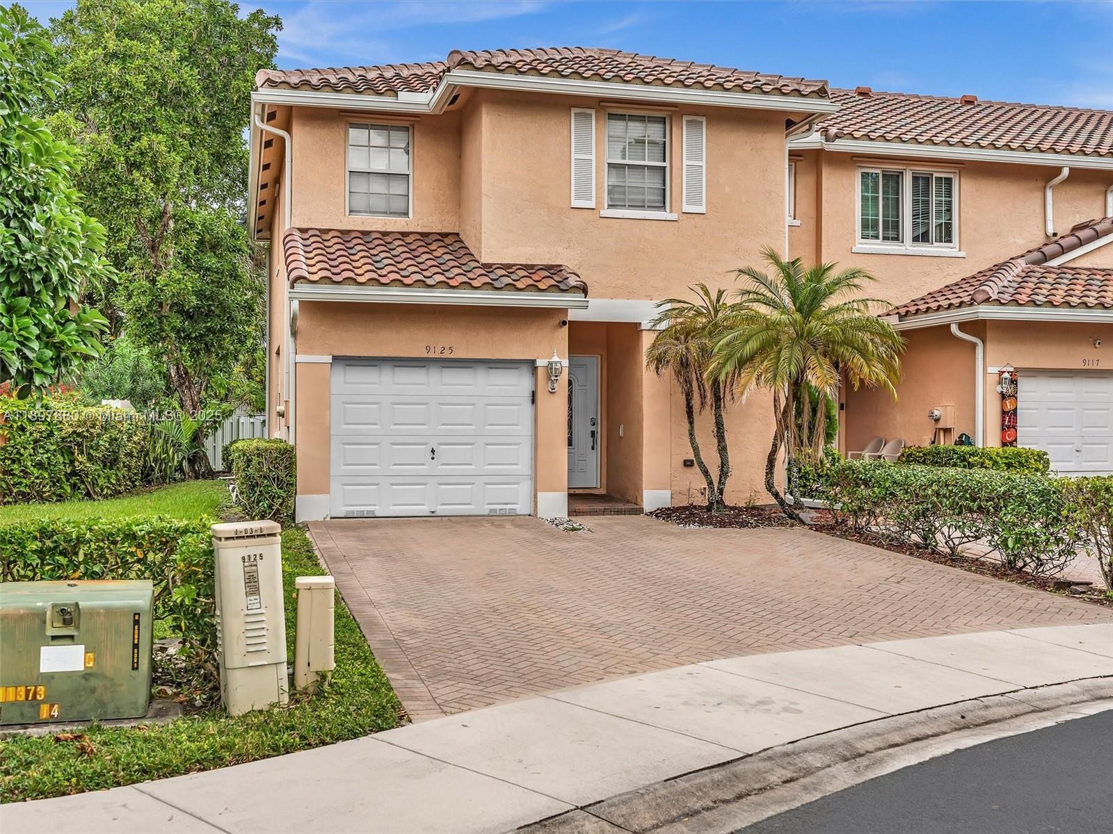 A two-story peach-colored townhouse with a white garage door and a paved driveway — 9125 NW 40th St, Sunrise FL 33351, SUNRISE, FL