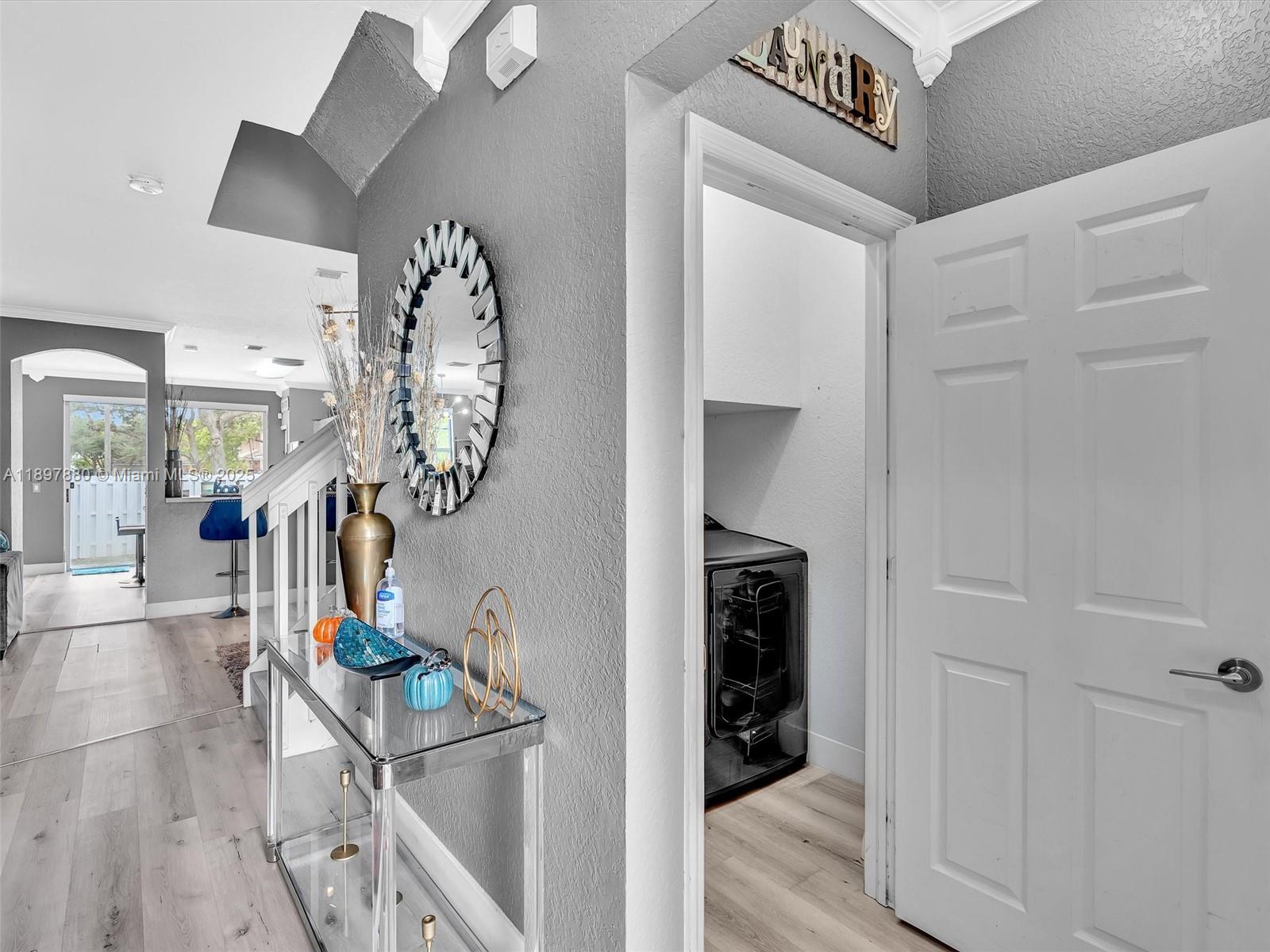 A hallway features a glass console table, a decorative mirror, and a laundry room entrance — 9125 NW 40th St, Sunrise FL 33351, SUNRISE, FL
