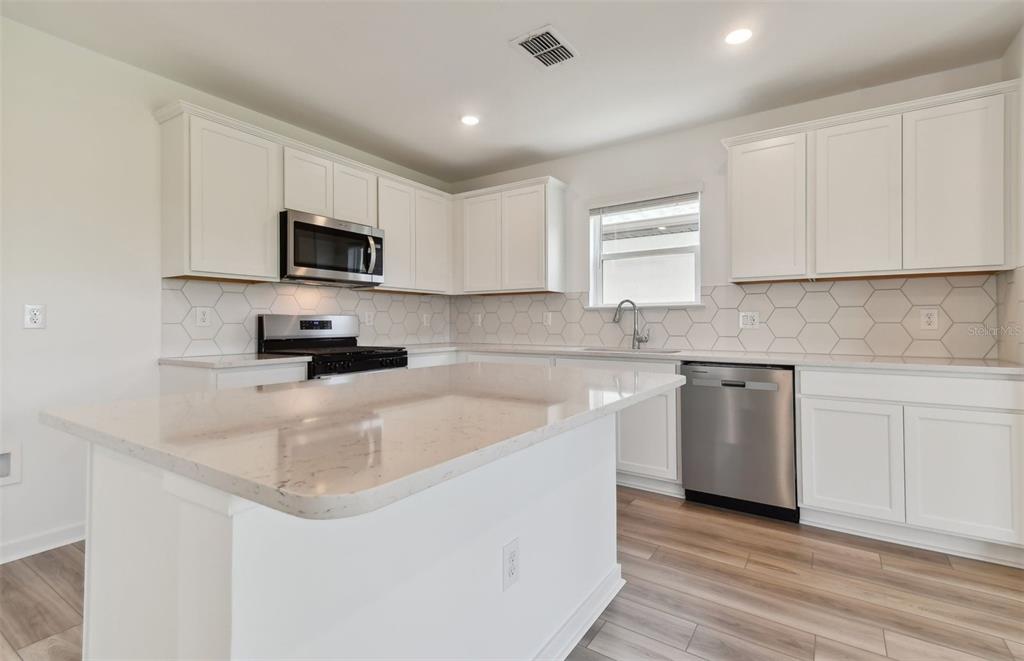A modern kitchen features white cabinets, a large island with quartz countertops, and stainless appliances — 33239 BINDING TIES LANE, WESLEY CHAPEL, FL
