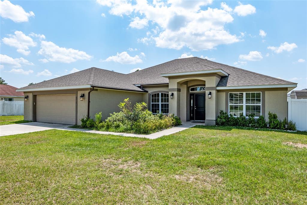 A single-story suburban house with a tan stucco exterior, a two-car garage, and a lawn — 10910 SW 41ST AVENUE, OCALA, FL