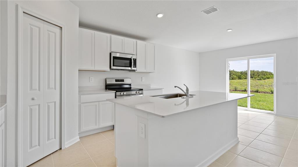 A modern kitchen features white cabinets, stainless steel appliances, a center island, and tile flooring — 391 ARTEMIS STREET, LAKE WALES, FL