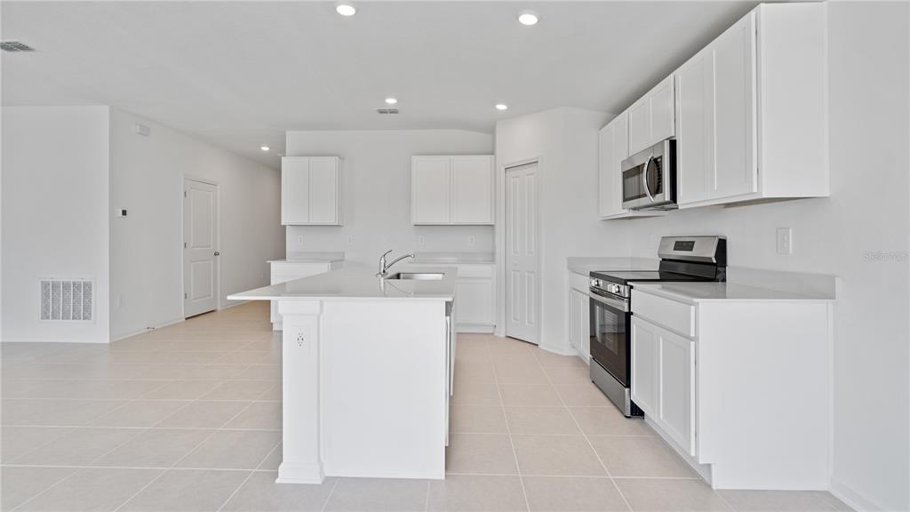 A modern kitchen features white cabinets, stainless steel appliances, a center island, and tile flooring — 391 ARTEMIS STREET, LAKE WALES, FL