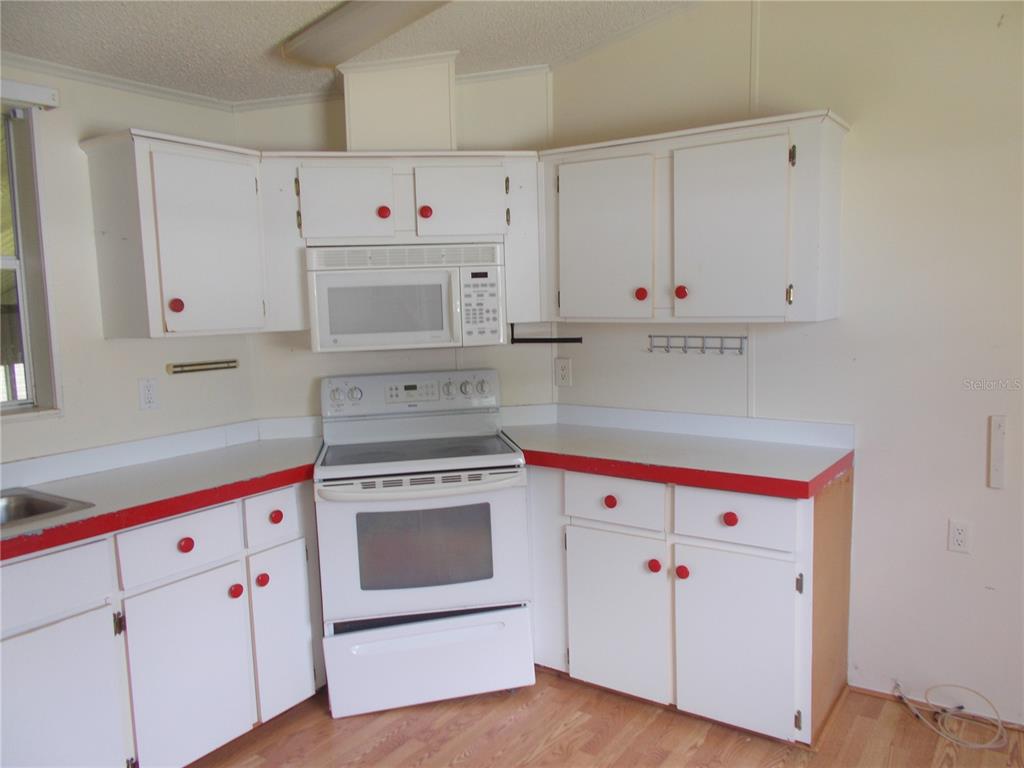 A kitchen features white cabinets with red knobs and red-trimmed countertops around a white stove — 5787 HOLIDAY PARK BOULEVARD, NORTH PORT, FL
