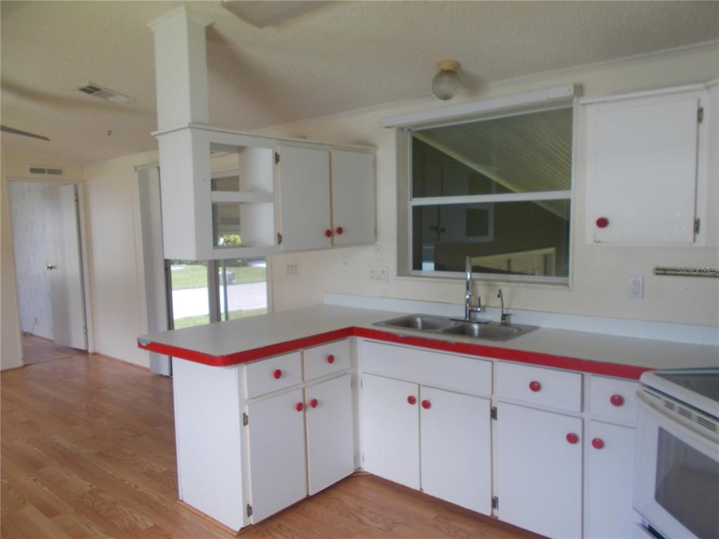 A kitchen features white cabinets with red knobs and red-trimmed countertops near a window — 5787 HOLIDAY PARK BOULEVARD, NORTH PORT, FL