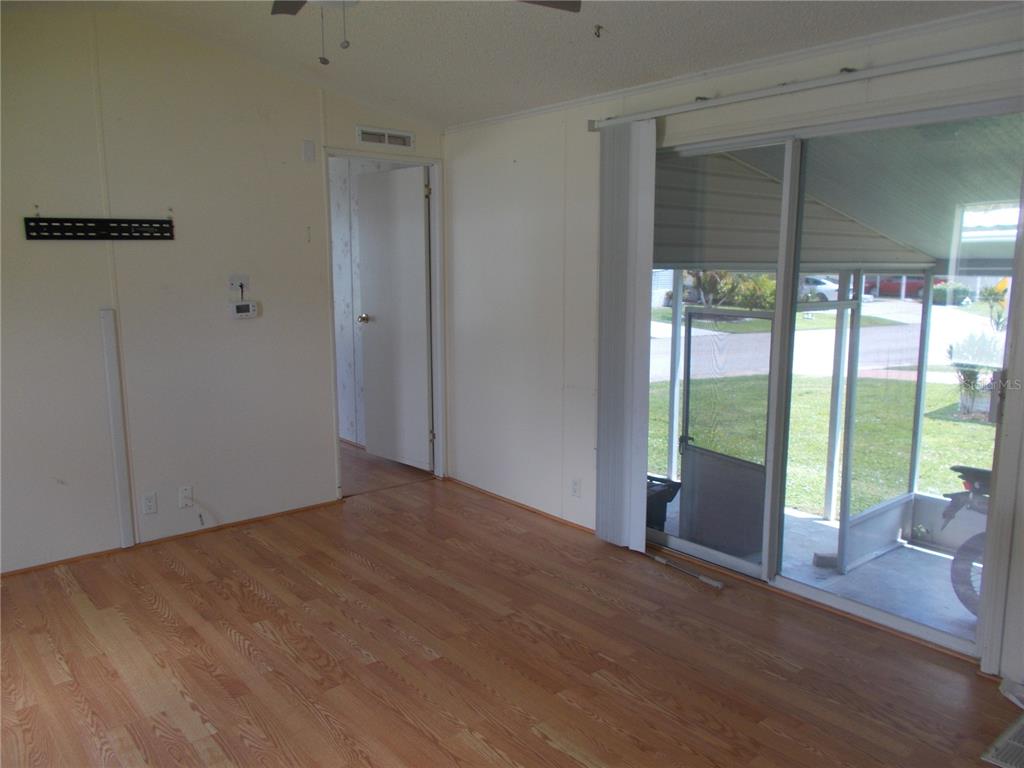 An empty room with wood-look flooring, a sliding glass door, and a doorway to another room — 5787 HOLIDAY PARK BOULEVARD, NORTH PORT, FL