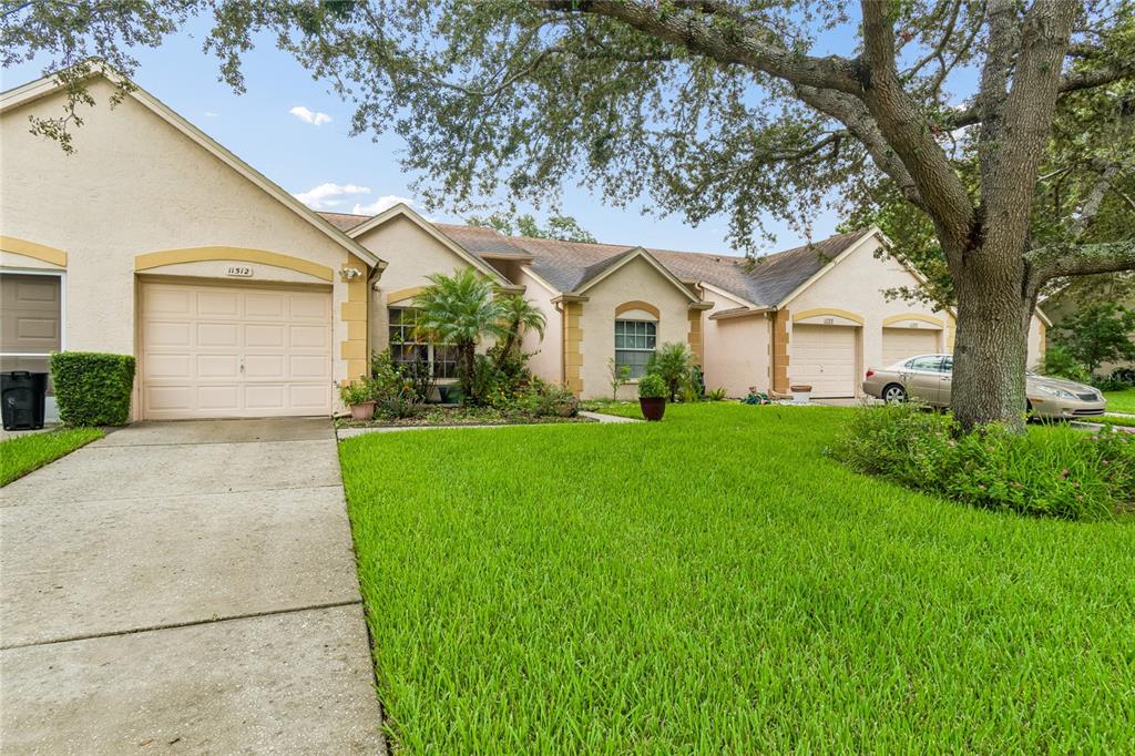 A single-story residential building with three garage doors and a large tree in the front yard — 11512 VERSAILLES LANE UNIT 11512, PORT RICHEY, FL