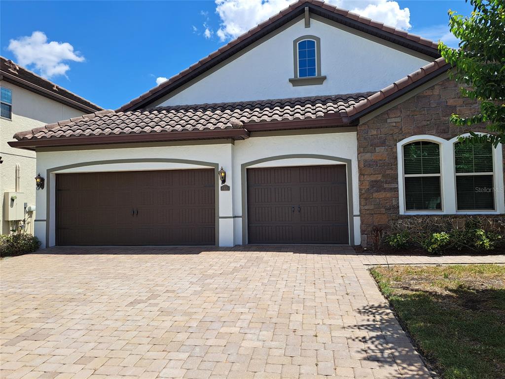 A two-car garage with brown doors and a stone-accented exterior under a tiled roof — 8420 MOREHOUSE DRIVE, ORLANDO, FL