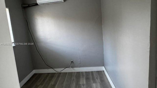 A small room with gray walls, wood-look flooring, and a wall-mounted air conditioning unit — FORT LAUDERDALE, FL
