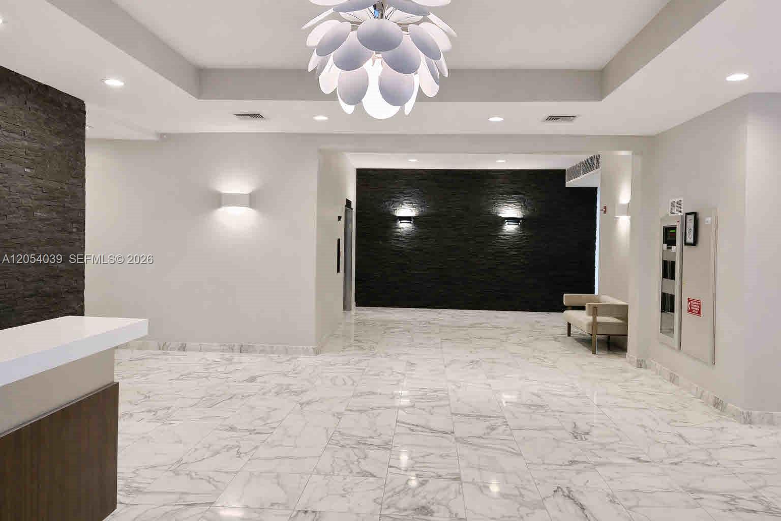 A modern lobby features a white marble floor, a large chandelier, and black stone walls — 9225 Collins Ave # 505, Surfside FL 33154, SURFSIDE, FL