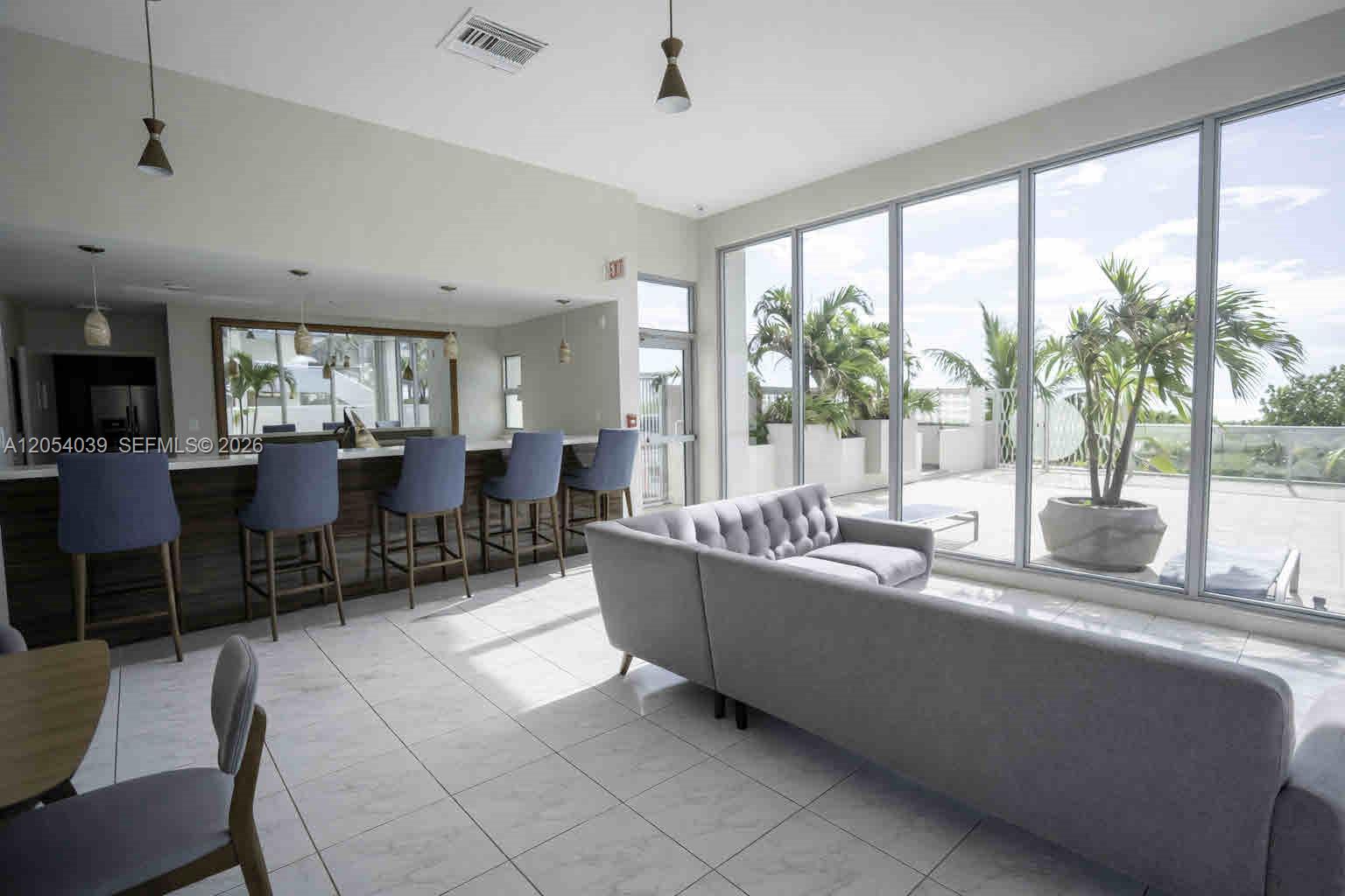 A modern lounge features a bar with blue stools, a gray sofa, and floor-to-ceiling windows — 9225 Collins Ave # 505, Surfside FL 33154, SURFSIDE, FL