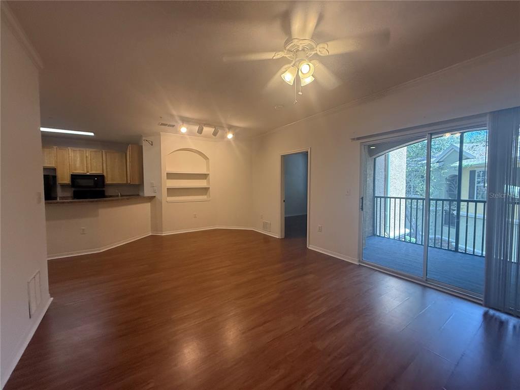 An open-concept living room with wood-look flooring, a ceiling fan, and a sliding glass door — 10121 COURTNEY PALMS BOULEVARD UNIT 201, TAMPA, FL