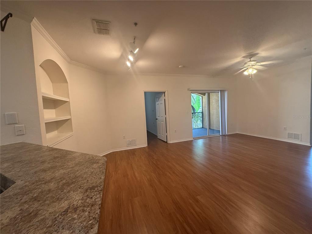 An open-concept living area features wood-look flooring, a built-in wall niche, and a sliding glass door — 10121 COURTNEY PALMS BOULEVARD UNIT 201, TAMPA, FL